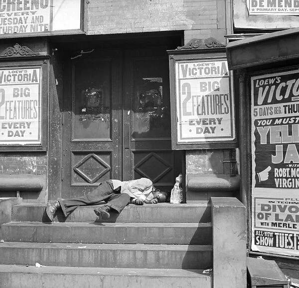 NEW YORK CITY, 1938. A man sleeping in the doorway of the Loews Victoria Theatre in Harlem