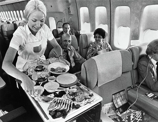 A Pan American flight attendant serves a meal to passengers on board. Photograph, c1975
