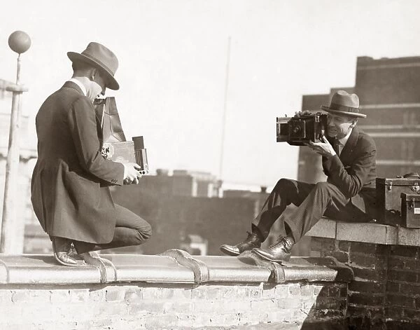 PHOTOGRAPHERS, C1920. Two photographers taking each others picture while perched on a roof