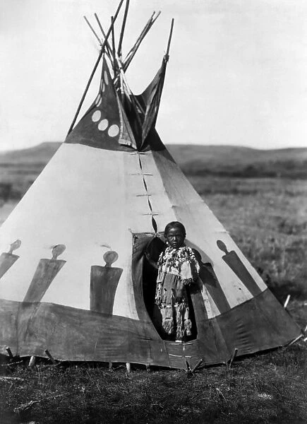 PIEGAN GIRL, c1910. The daughter of a Piegan Blackfoot chief, standing at her tepee. Photograph by Edward Curtis, c1910