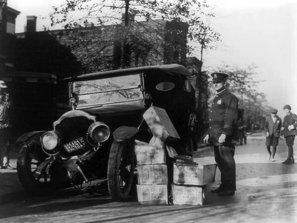 PROHIBITION, 1922. A police officer standing beside a wrecked car and cases of moonshine