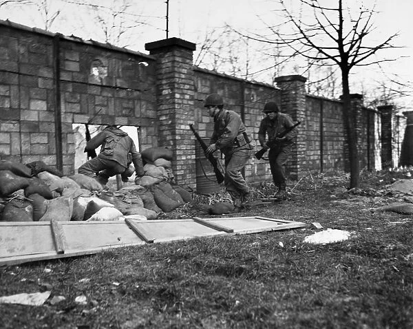 A raiding party of soldiers from the 143rd Infantry Regiment, 36th Division, U. S. Seventh Army, dash through a sandbagged hole in a brick wall that opens onto the Moder River; the soldiers were raiding the enemy-held bank of the river opposite Haguenau, France, in order to bring back prisoners. Photographed 3 March 1945