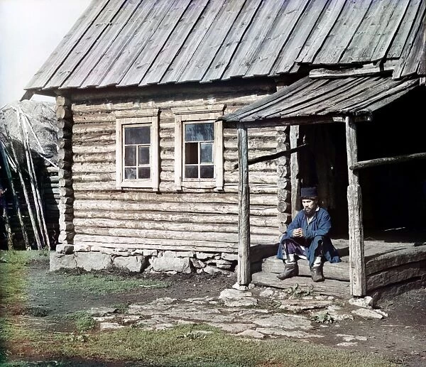 RUSSIA: LOG CABIN, 1910. A Bashkir man sitting on the steps of a log cabin in the