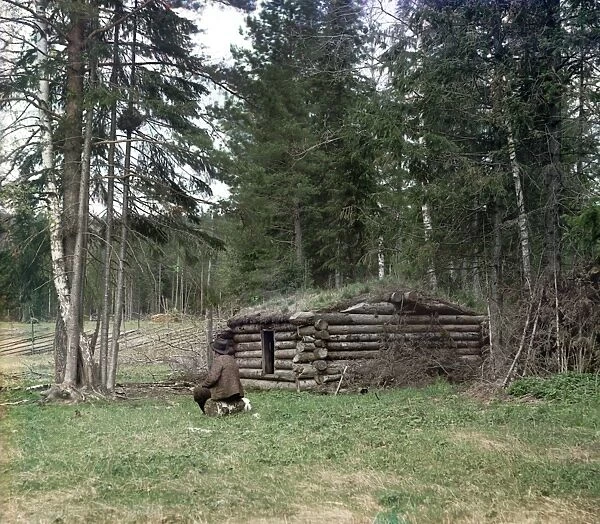 RUSSIA: LOG CABIN, 1912. A Bashkir man sitting on a log beside a small log cabin