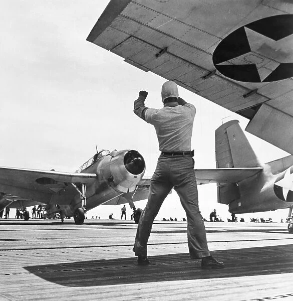 A signal officer directs a fighter plane on board the USS Yorktown in a scene from the American propaganda film, The Fighting Lady, 1944