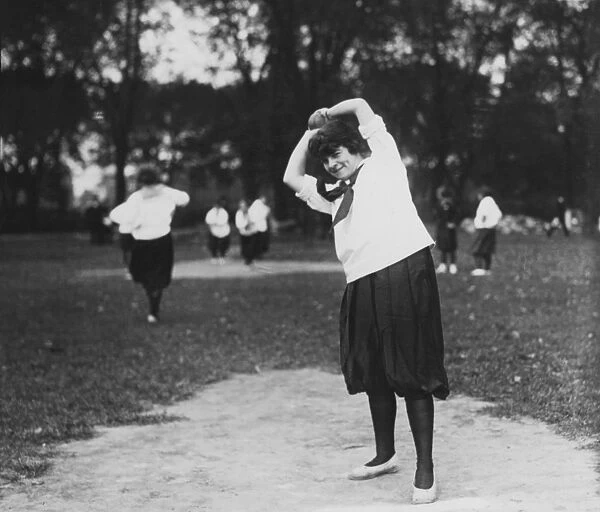 SOFTBALL GAME. A woman on the pitchers mound preparing to throw the ball during a softball game, c1920
