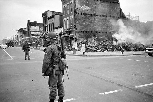 A soldier standing guard in a street in Washington, D. C. across from the ruins of buildings destroyed in the rioting that followed the assassination of Martin Luther King, Jr. Photographed by Warren K. Leffler, 8 April 1968