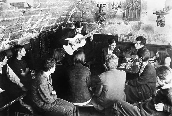 Students listening to a guitar player at a cafe in Paris, France. Photograph, c1960