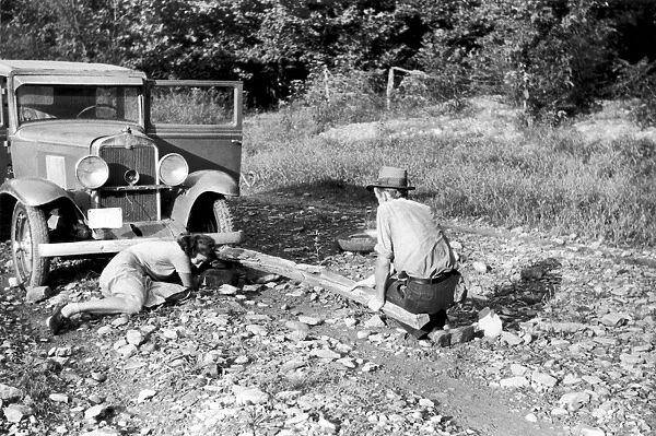 TIRE CHANGING, 1940. Photographer Marion Post Wolcott changing a flat tire on a borrowed car