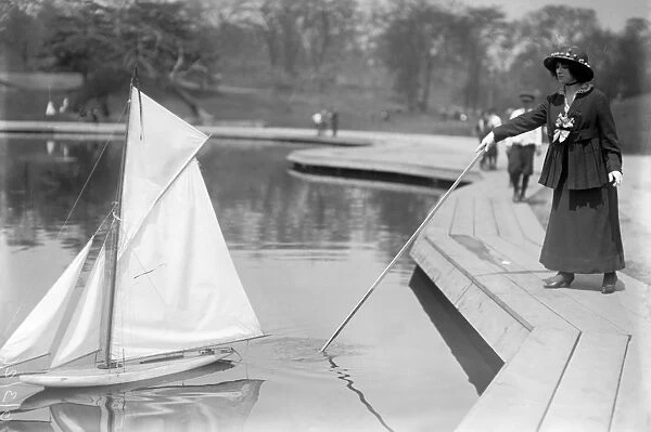 TOY YACHT RACE, C1912. Woman pushing off a toy yacht (gaff cutter) at the Conservatory