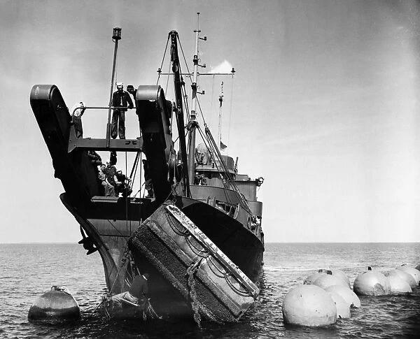 A U. S. Navy ship laying an anti-torpedo net at the mouth of the harbor of Norfolk, Virginia. Photographed March 1944