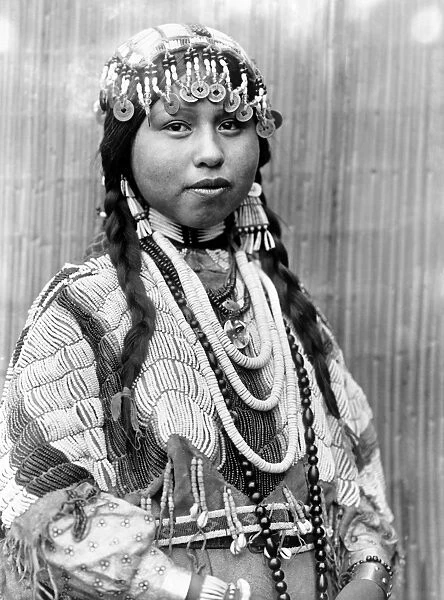 WISHRAM BRIDE, c1910. Half-length portrait of a Wishram (Tlakluit) bride with braids, wearing a beaded headdress with Chinese coins, dentalium shell earrings and beaded buckskin dress, with beads around her neck. Photographed by Edward S. Curtis, c1910