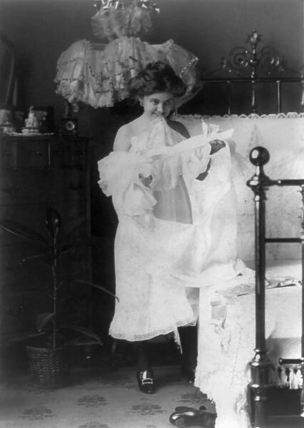 WOMAN: NIGHTGOWN, c1900. A woman putting on a nightgown before going to bed. Photograph