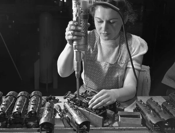Worker Stephanie Cewe using an electric screwdriver to assemble locomotives for toy trains at a factory in New Haven, Connecticut, shortly before the plant was converted to the manufacture of parachute flare casings during World War II. Photographed by Howard R. Hollem, 1942