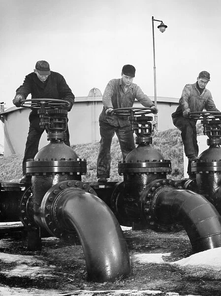 Workers at an Atlantic coast seaport in the United States regulate the flow of oil onto tankers bound for armed forces during World War II. Photographed c1944