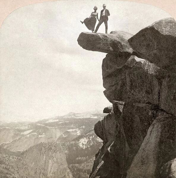 YOSEMITE VALLEY, c1902. A couple standing on a rock at the top of the cliff with the woman raising her right leg as though she is stepping off of Glacier Point Rock in Yosemite National Park, California. Stereograph, c1902