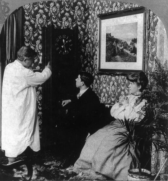 YOUNG COUPLE, c1904. A man in a nightgown pointing out the late time of 1: 30 am to a young couple