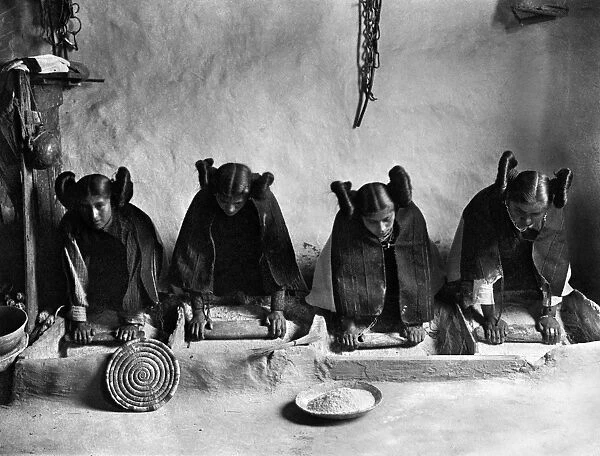 Four young Hopi women in Arizona grinding grain at the mealing trough. Photographed by Edward S. Curtis, c1906