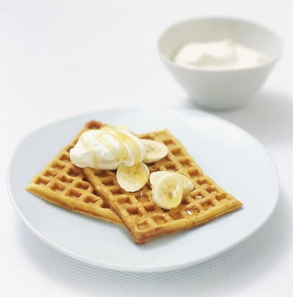 Belgian waffles served with whipped cream, banana slices and golden syrup, high angle view
