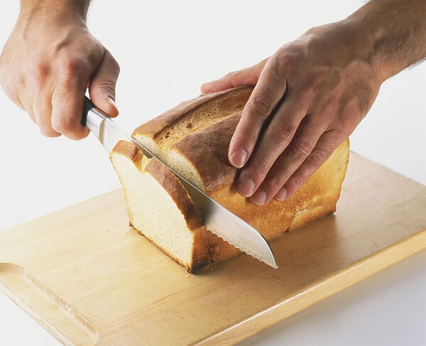 Close-up of slicing a loaf of white bread using a sharp serrated bread knife