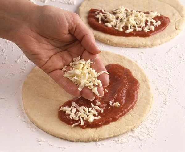 Making calzone pizza, sprinkling cheese on top of tomato sauce on pizza base