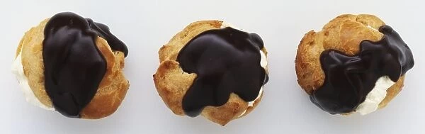Above view of three profiteroles, choux pastry filled with cream and coated in chocolate sauce