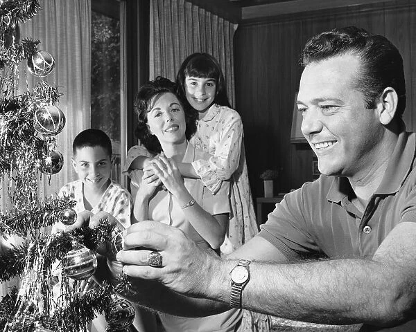 Family in living room, father decorating Christmas tree
