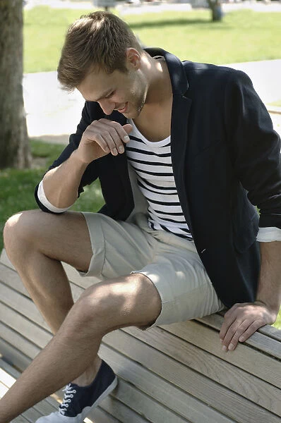 Young man in casual outfit sitting on a park bench in a park