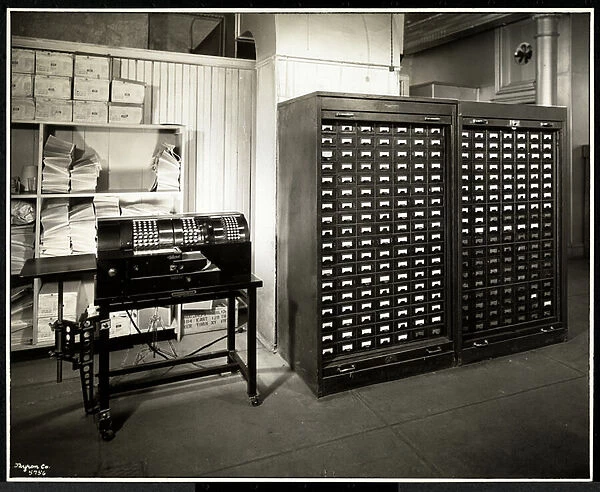 Possibly an adding machine and a filing cabinet with small drawers in the office of