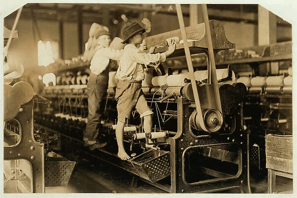 Small boys climbing on spinning frame to mend broken threads and replace empty bobbins at Bibb Mill