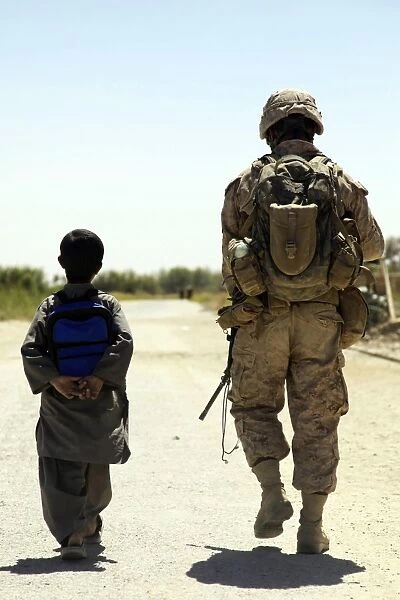 Rear view of U. S. Marine walking through Nawa bazaar with an Afghan boy in Afghanistan