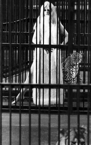 Brigitte Bardot French actress in skin tight catsuit with fur cape standing beside cage