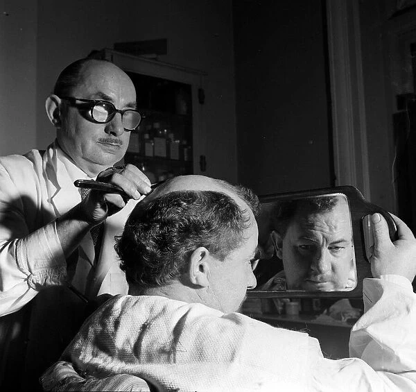 Leo McKern looks at his reflection in a mirror after getting a special hair do for a