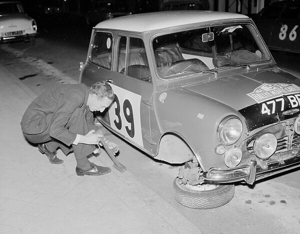 Rally driver raymond Baxter repalces the wheel of his Mini car which was removed by some