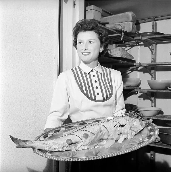 Woman holding fish on a platter. 1957 A17a
