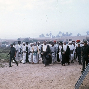 Soldiers with Omani elders walking in the sand. in Oman