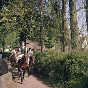 Women and children riding horses along a country lane