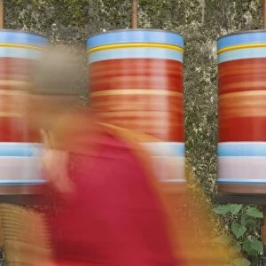 Buddhist monk passing prayer wheels