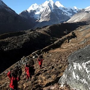 Three Buddhist monks carry firewood high above the mountain village of Khare