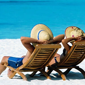 Couple lying in deck chairs on beach, The Maldives, Indian Ocean, Asia
