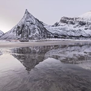 Snowy peaks reflected in the frozen sea surrounded by sandy beach at dawn, Ersfjord