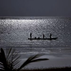 Three men pole a dugout canoe by moonlight in shallow water along Diani Beach