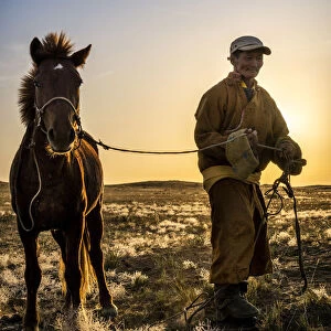 Mongolian shepherd wearing traditional dress in steppe of Gobi desert with his hourse