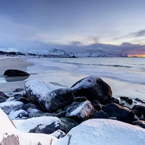 Romantic sky at sunset over the cold arctic sea washing the frozen Bovaer beach, Skaland, Senja, Troms county, Norway