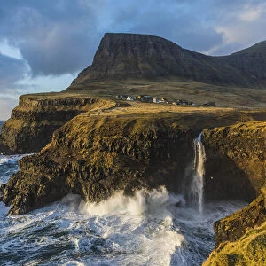 The village of Gasadalur and its waterfall, at sunset, while they are hit by strong winds. Vagar, Faroe Islands