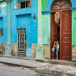 Two young girls peaking through the door of their house in Centro Habana Province, Havana