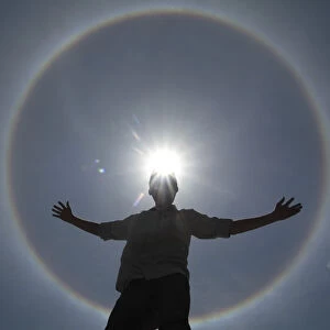 A man poses for photos as solar halo is seen in the sky of Brasilia