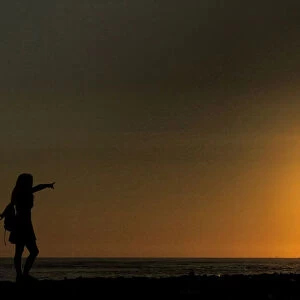 A man takes a photo of a woman on a beach at sunset in Lima