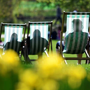 People are silhouetted against the fabric of deckchairs as they enjoy the sunshine in St