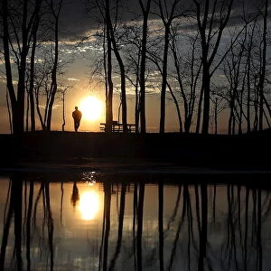 People stand and watch the sun set as they are reflected in a puddle at Presque Isle
